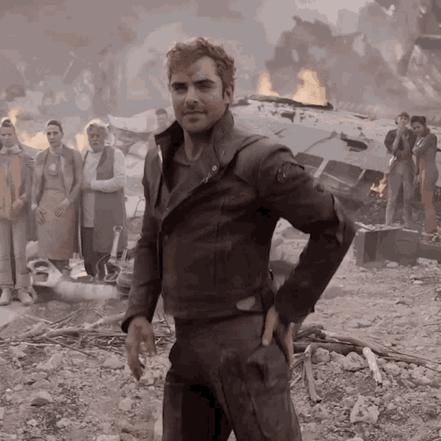 a man in a leather jacket is standing in front of a fire