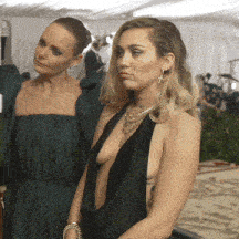 a woman in a green dress is standing next to a woman in a black dress with a plunging neckline