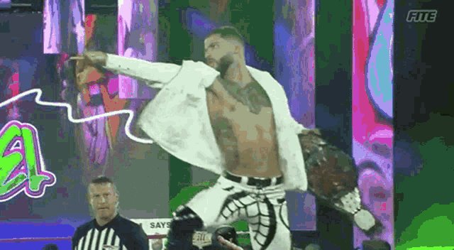 a man in a white suit is jumping in the air while holding a wrestling belt .