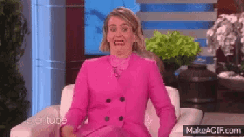 a woman in a pink suit is sitting in a chair with her mouth open .
