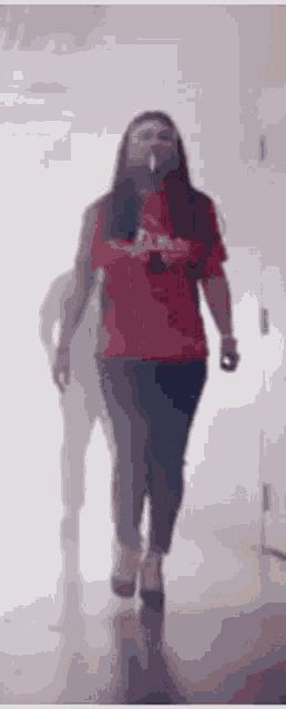 a woman in a red shirt is walking down a hallway while smoking a cigarette .