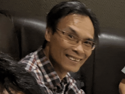 a man wearing glasses and a plaid shirt is smiling while sitting in a chair .