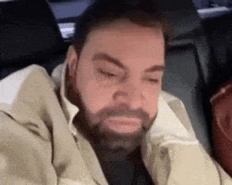 a man with a beard is sitting in the back seat of a car and making a sad face .