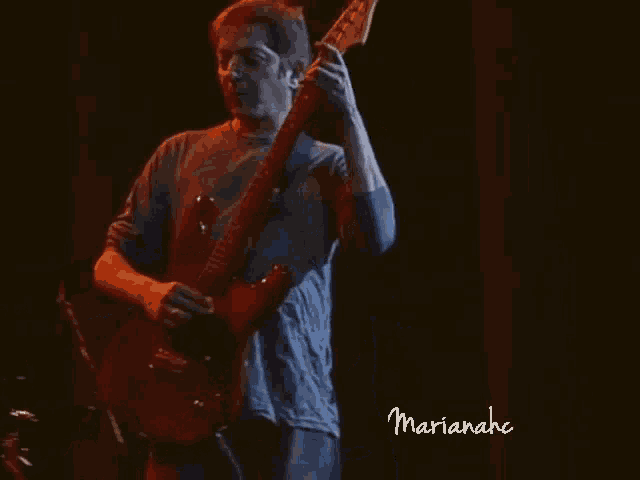 a man in a blue shirt is playing a guitar with the name marianahc on the bottom right