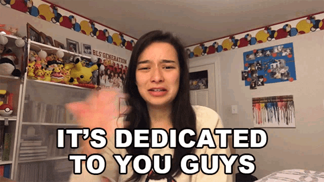 a woman says it 's dedicated to you guys in front of a shelf full of stuffed animals