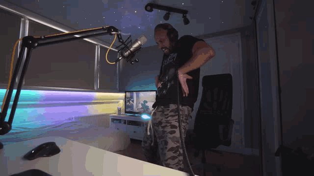 a man playing a guitar in front of a microphone in a room with two monitors and a mouse