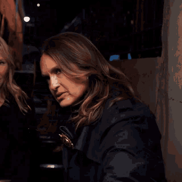 a woman in a blue trench coat stands next to another woman in a black shirt