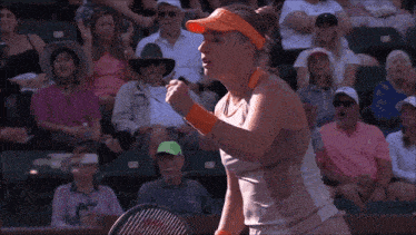 a woman wearing an orange visor stands in front of a crowd at a tennis match