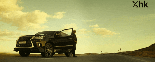 a man standing next to a black car with a license plate that says hk