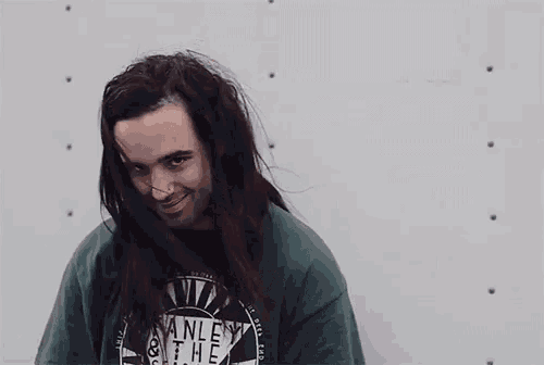 a man with long hair is wearing a green stanley t-shirt