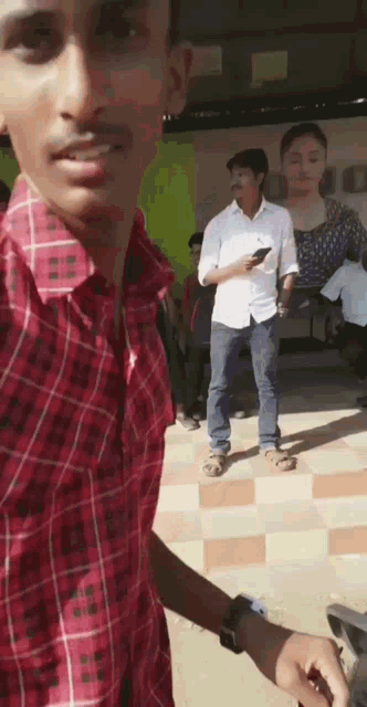 a man in a red plaid shirt is standing in front of a group of people and holding a cell phone .