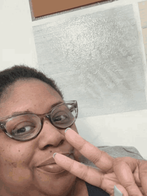 a woman wearing glasses making a peace sign