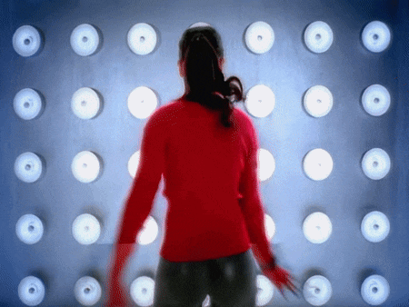 a woman in a red sweater is dancing in front of a wall of lights
