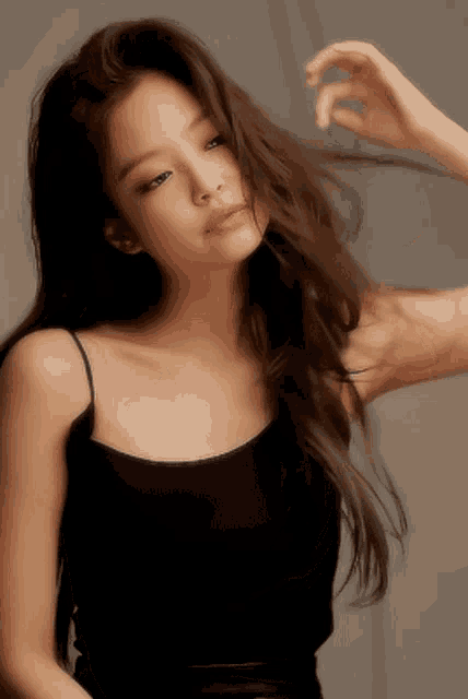 a woman in a black tank top holds her hair