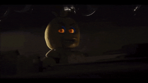 a yellow stuffed animal with glowing eyes is sitting in the dark