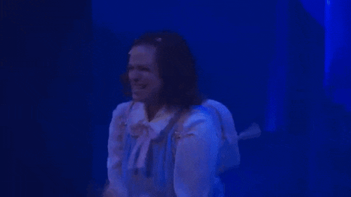 a woman is standing on a stage with her arms outstretched in a dark room .