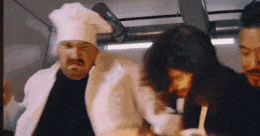 a man in a chef 's hat is standing next to a woman and a man in a black shirt .