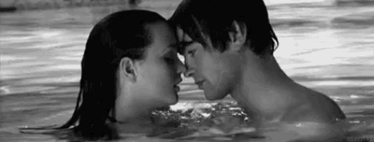 a black and white photo of a man and a woman kissing in a swimming pool .