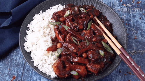 a bowl of chili pepper chicken and rice with chopsticks in it