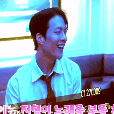 a man in a white shirt and tie is smiling in front of a sign with c127c009 on it