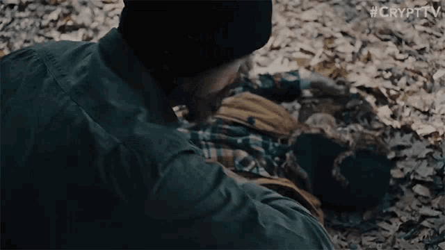 a man in a black hat is laying on the ground next to a dead person .