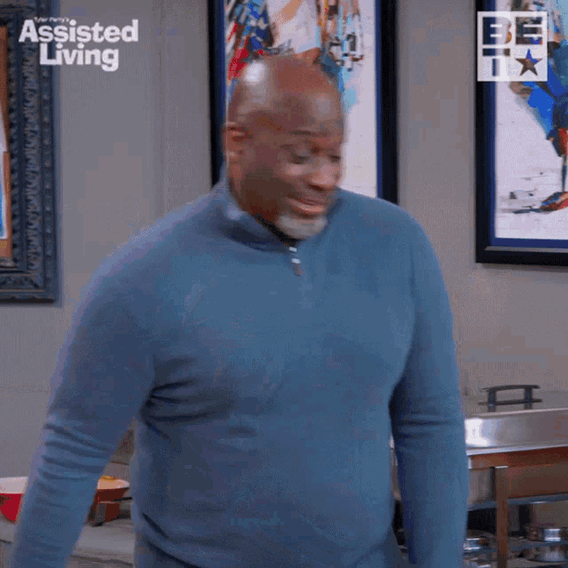 a man in a blue sweater is standing in front of a wall that says assisted living on it