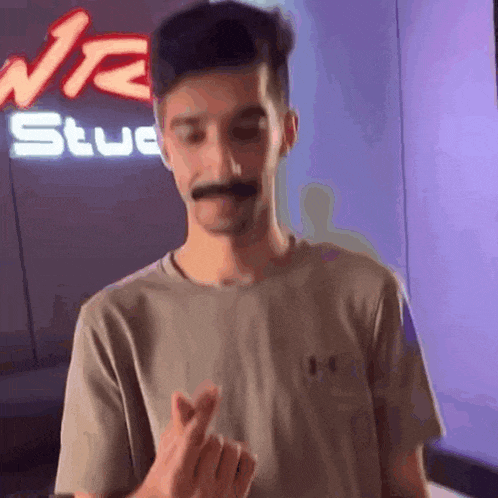 a young man with a mustache is making a heart shape with his fingers .