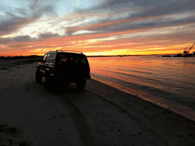 a black jeep is parked on a beach at sunset