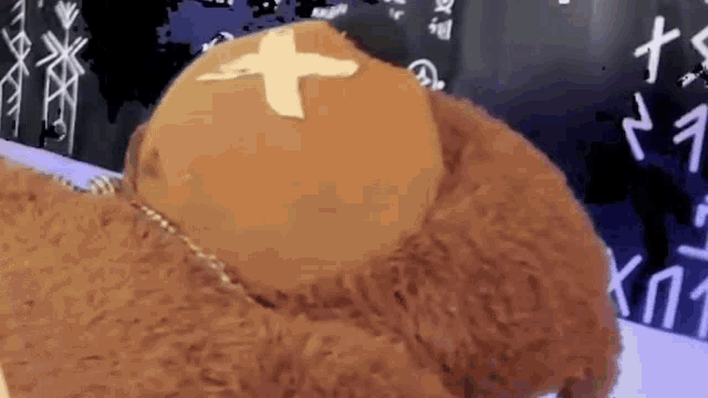a teddy bear with a cross on its head is sitting on a table .