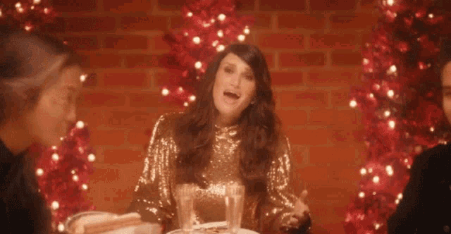 a woman in a sequined dress is sitting at a table with a christmas tree in the background