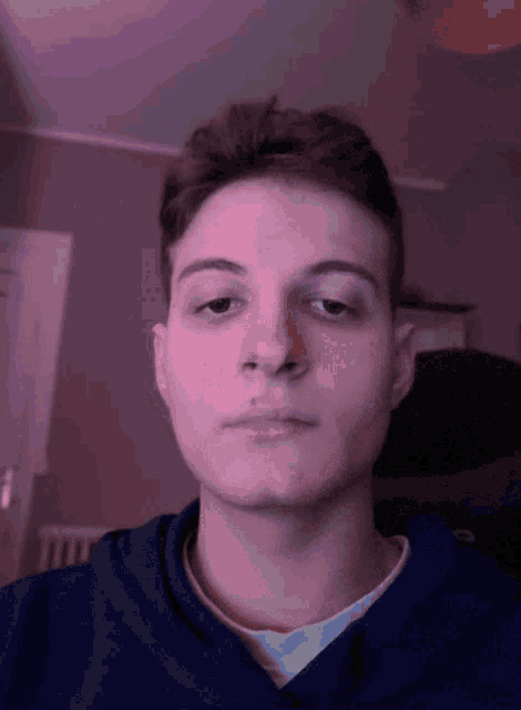 a young man in a blue shirt looks at the camera with his eyes closed