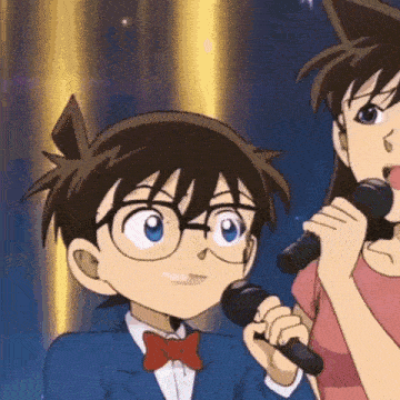 a boy in a suit and bow tie is singing into a microphone next to a woman in a pink shirt .