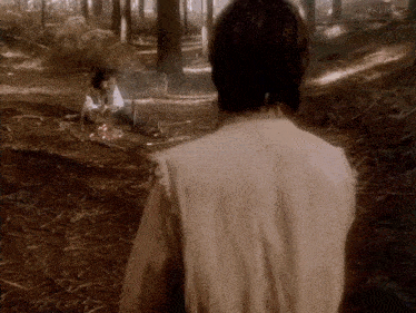 a man is standing in the woods looking at another man .