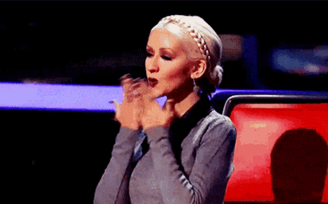 a woman in a gray sweater is clapping her hands in a dark room