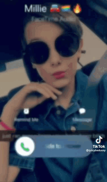 a woman wearing sunglasses and a denim shirt is sitting in a car talking on a cell phone .