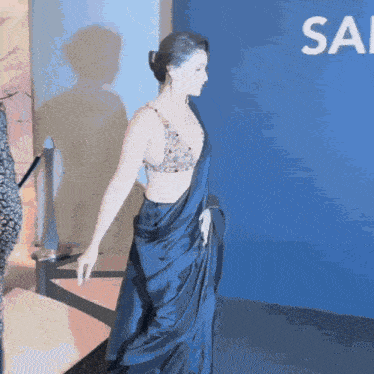 a woman in a blue dress is walking in front of a sign that says sa
