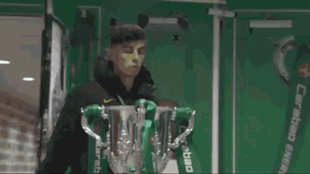a man in a black jacket is holding a trophy in a green room .