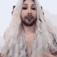 a man with a beard and long white hair is wearing a wig and looking at the camera .
