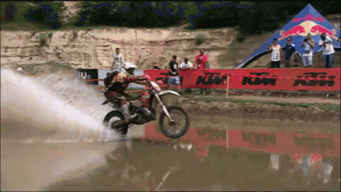 a man riding a dirt bike in the water with a ktm sign in the background
