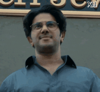 a man wearing glasses and a blue shirt stands in front of a sign that says xhk