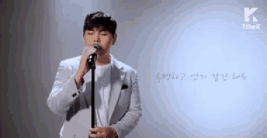 a man in a suit is singing into a microphone while standing in front of a white board .