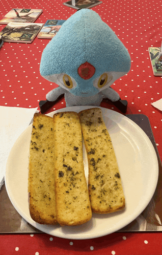 two garlic bread sticks on a white plate with a stuffed animal in the background