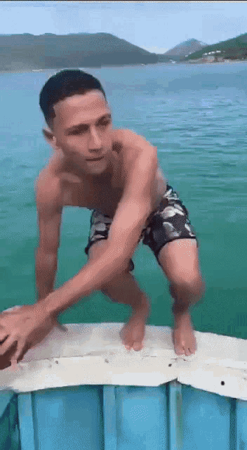 a shirtless man in shorts is standing on a dock in the water