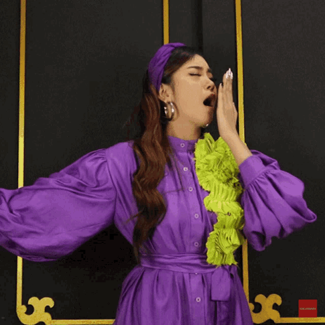 a woman in a purple dress is yawning with her hand on her mouth