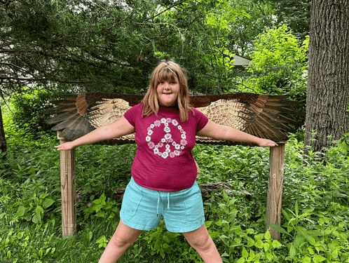 a girl with a peace sign on her shirt stands in front of a bird sculpture