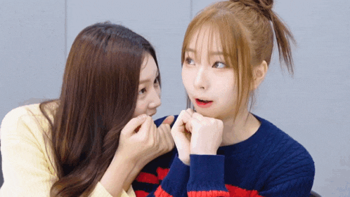 two girls are looking at each other and one is wearing a blue sweater