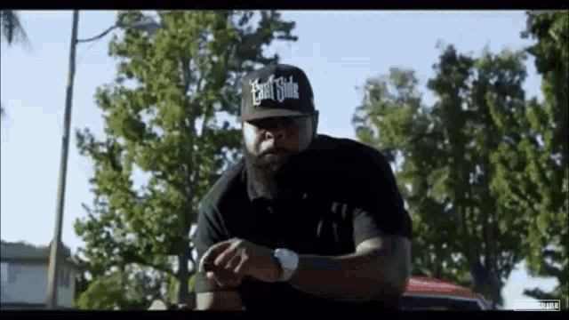 a man wearing a east side hat is standing in front of trees .