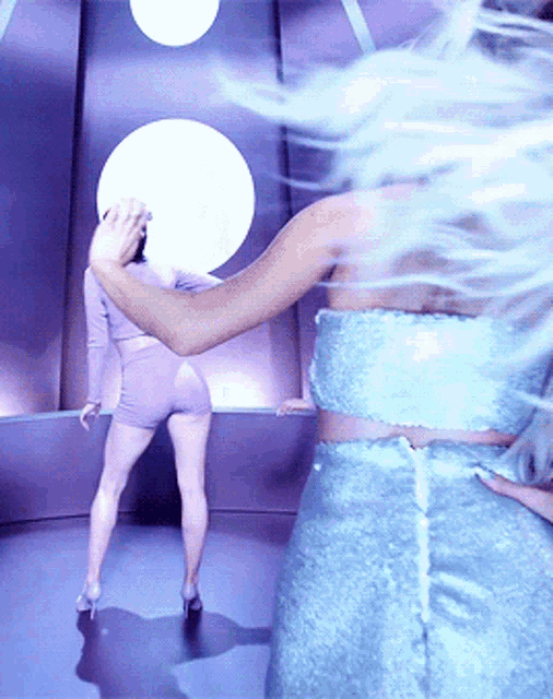 a woman in a blue dress is standing next to another woman in purple shorts