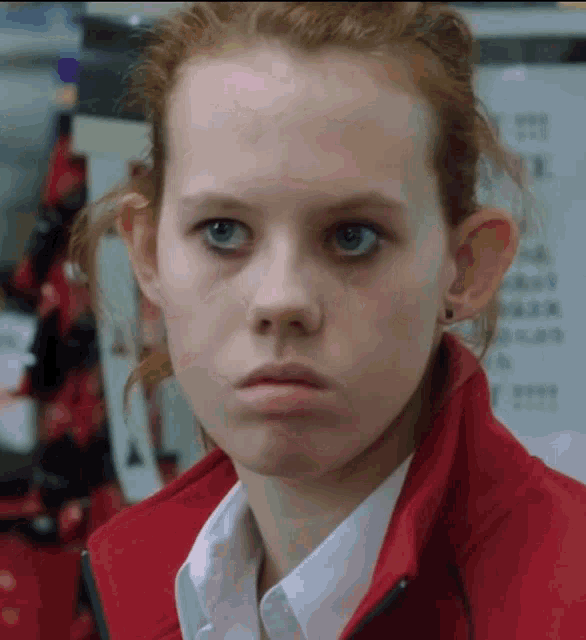 a girl with red hair and blue eyes is wearing a red jacket and white shirt
