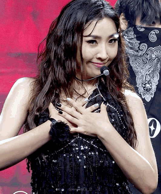 a woman in a black sequined dress with her hands on her chest